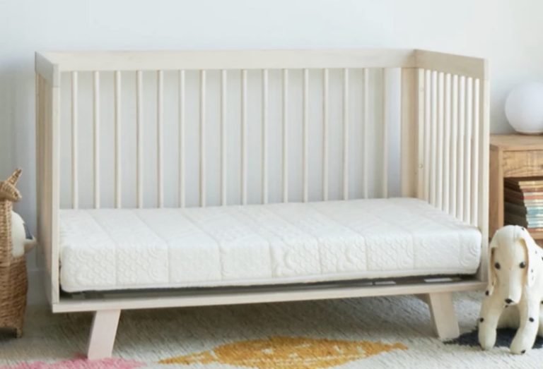 The Brentwood Home EcoAir Crib Mattress on a light tan wood frame.